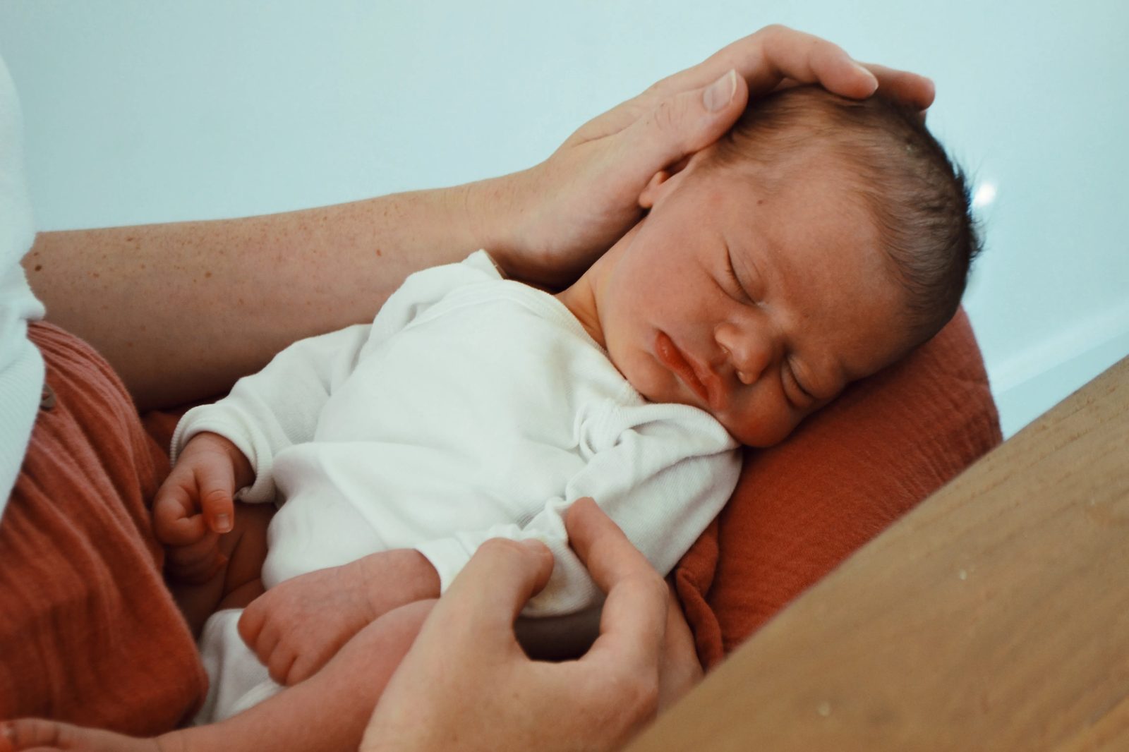 Slapende pasgeboren baby in een witte body, rust op de schoot van een ouder